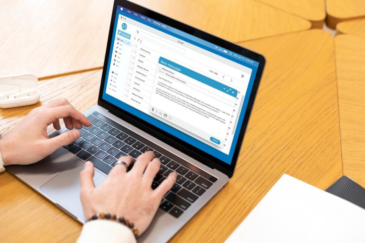 A person types on a laptop, composing an email. The screen displays a message window and a list of email contacts.
