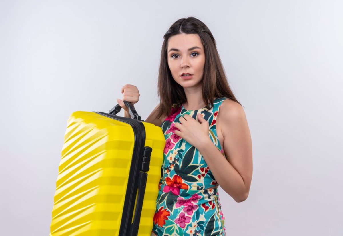 A woman in a colorful floral dress holds a bright yellow suitcase, posing against a white backdrop.