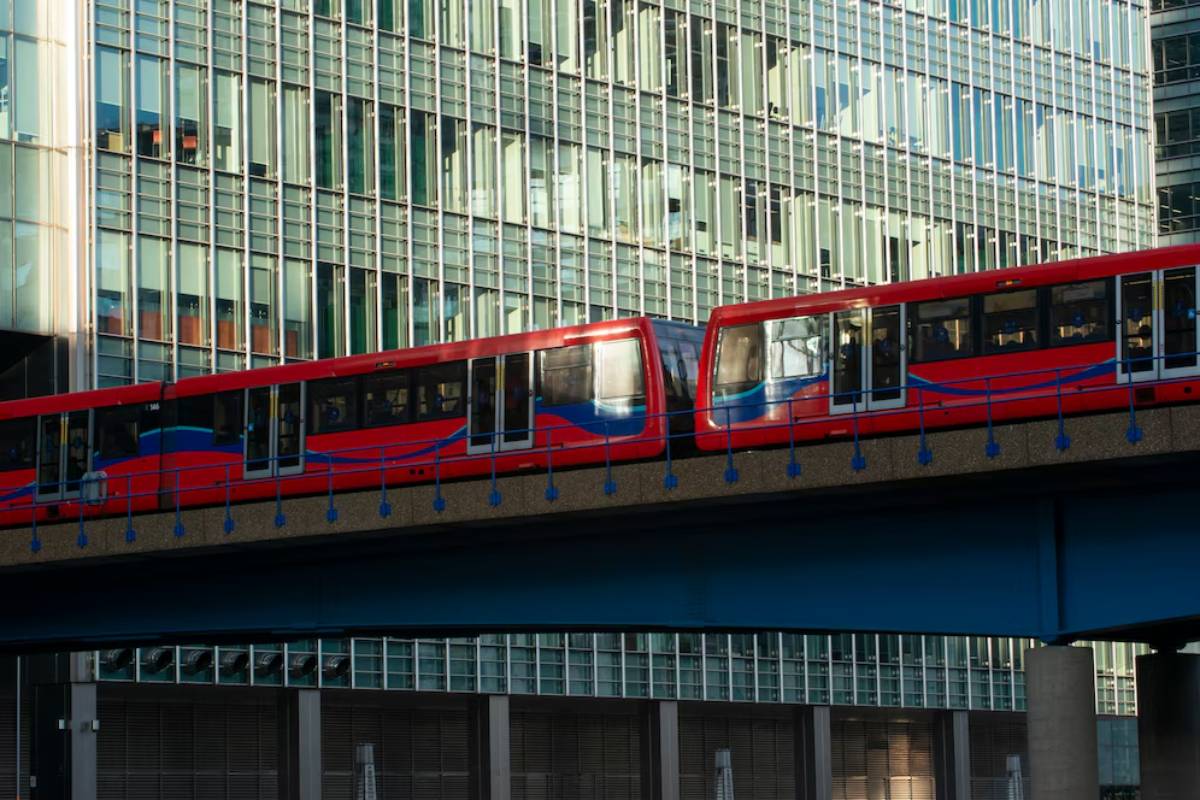 A red and blue elevated train travels along a bridge against a backdrop of modern glass skyscrapers.