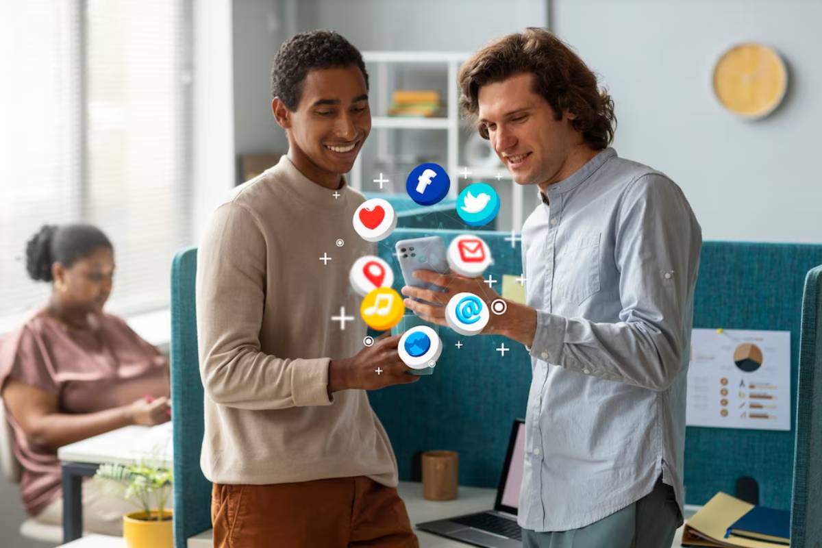 Two people collaborate in an office, discussing a smartphone while social media icons hover above their hands, symbolizing digital interaction.