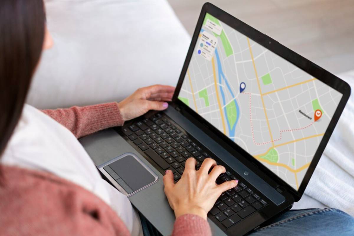 A person using a laptop to view a map with location markers and a route highlighted, sitting comfortably on a couch.