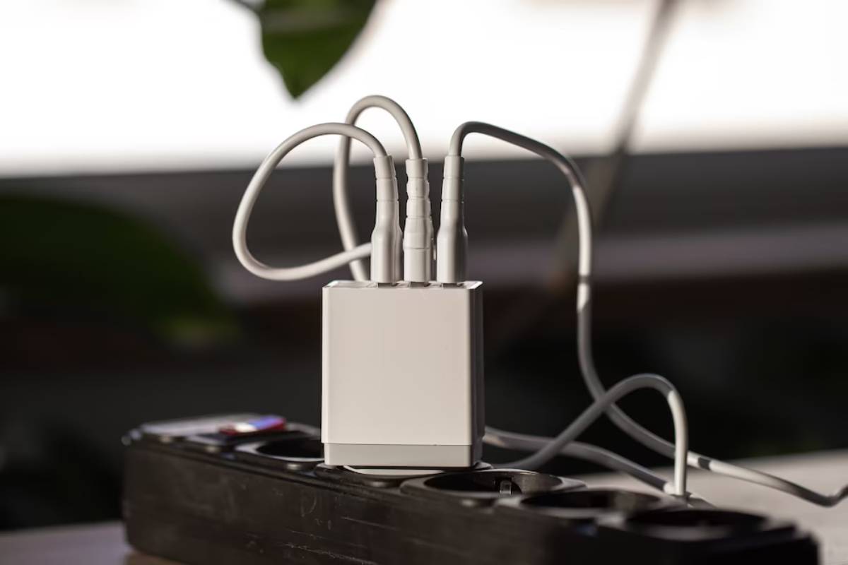 A white multi-port charger with several connected cables, placed on a black power strip against a softly blurred background.