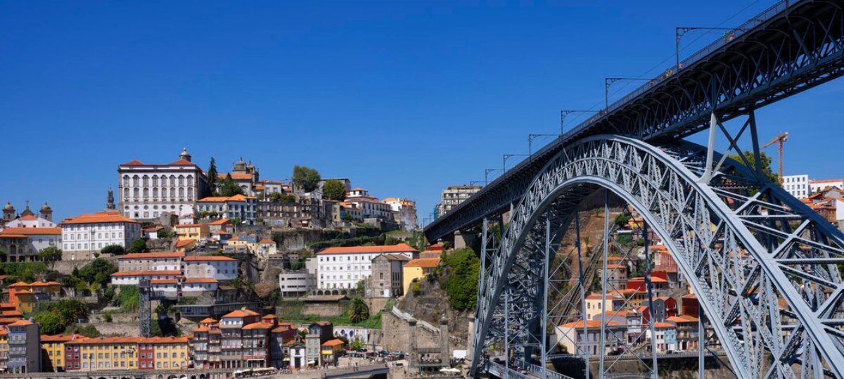 A scenic view of Porto, Portugal, featuring colorful hillside buildings and the iconic Dom Luís I Bridge against a clear blue sky.