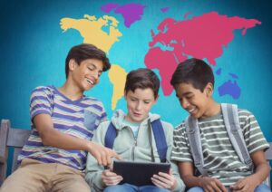 Three students are engaged in a discussion while examining a tablet, with a colorful world map in the background.