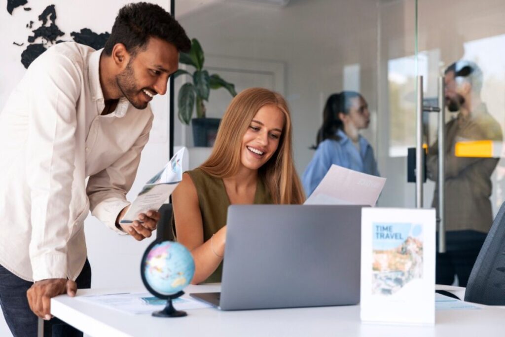 A woman and a man discuss travel plans at a modern office desk, with a globe and travel brochures on display.