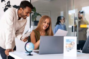 A woman and a man discuss travel plans at a modern office desk, with a globe and travel brochures on display.