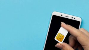 A person holds a SIM card near a smartphone's screen against a blue background, ready to insert it into the device.