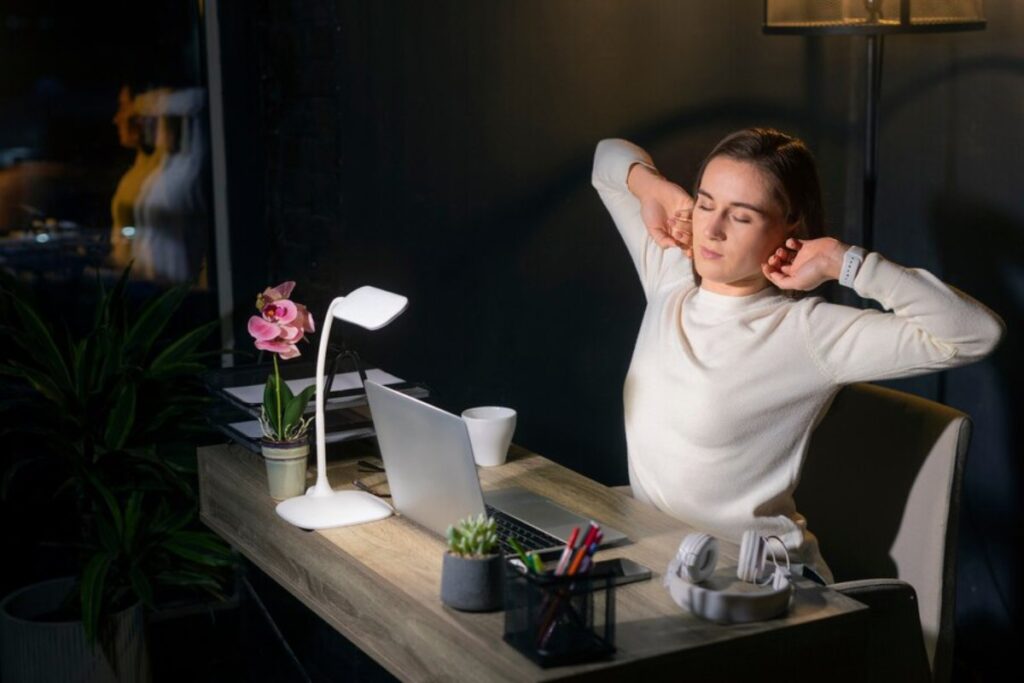 A cozy desk setup in a dimly lit room, featuring a laptop, plants, a desk lamp, and a cup, evoking a calming workspace atmosphere.